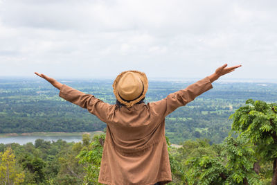 Rear view of man with arms outstretched standing against sky