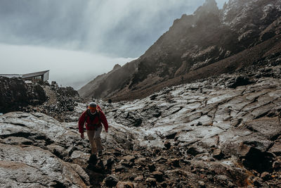 Rear view of person on rock in mountains against sky