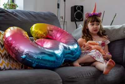 Portrait of cute girl on sofa with a doll and a balloon