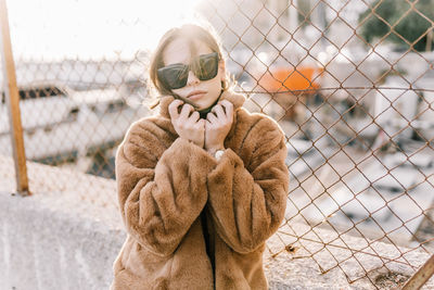 Young woman standing by fence during winter