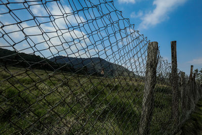 Barbed wire fence on field against sky