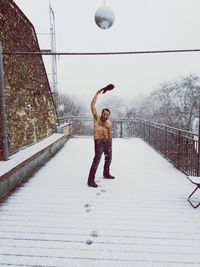 Full length of shirtless man throwing shirt in snow