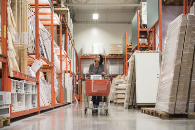 Mature female customer looking up while pushing shopping cart in hardware store