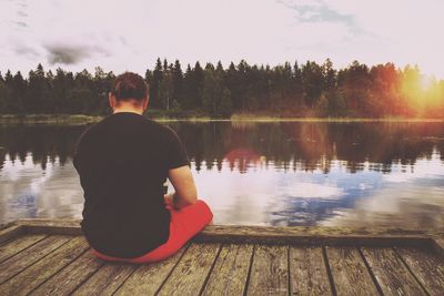 Rear view of woman sitting by lake against sky