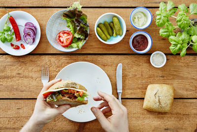 Directly above shot of cropped hands holding burger on table