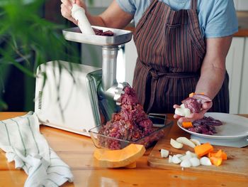 An elderly woman is busy in the kitchen twisting meat through a meat grinder. healthy homemade food.