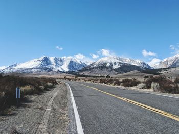 Empty road leading towards mountains against blue sky