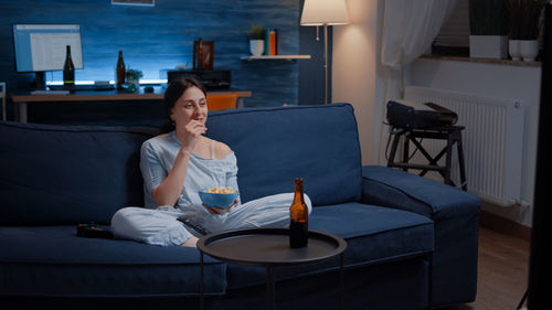 Smiling woman eating popcorn sitting on sofa