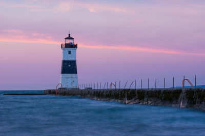 Lighthouse by sea against sky during sunset