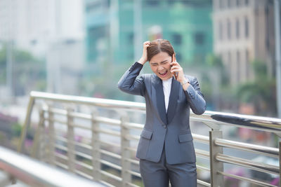 Angry businesswoman talking on mobile phone on bridge in city