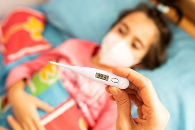 Close-up of woman hand holding thermometer over daughter lying on bed