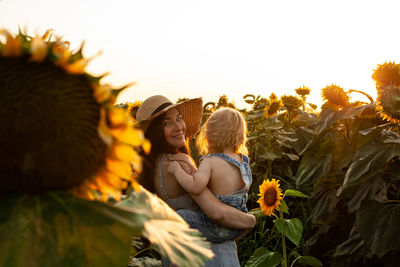 Beautiful mother holds a little son in her arms in a field of sunflowers at sunset