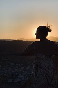 Rear view of woman looking at cityscape against sky during sunset