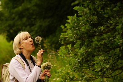 Woman blowing dandelion seed while standing in park