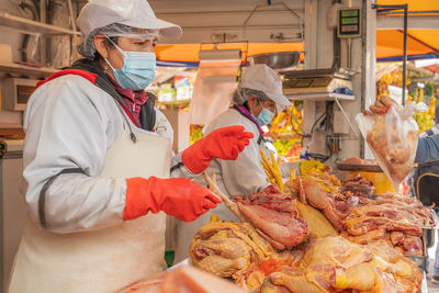 Peruvian female sellers in face masks and aprons standing behind counter with raw chicken meat during work on itinerant fair