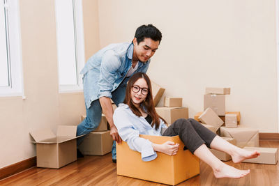 Man pushing girlfriend sitting in cardboard box at home