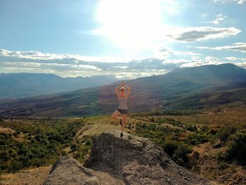 Full length of woman practicing tree pose on rock against sky