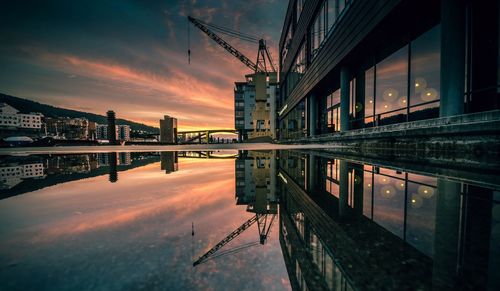 Crane and buildings reflecting on puddle against orange sky