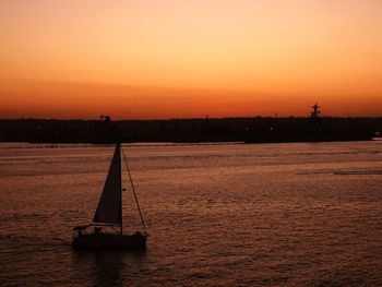 Silhouette sailboat on sea against orange sky