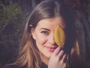 Close-up portrait of young woman holding leaf