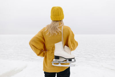 Woman in warm clothing standing with ice skates in front of winter sea