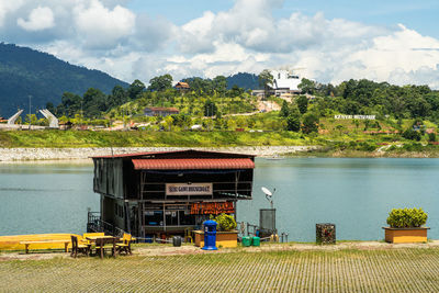 Plants by house against lake and buildings against sky