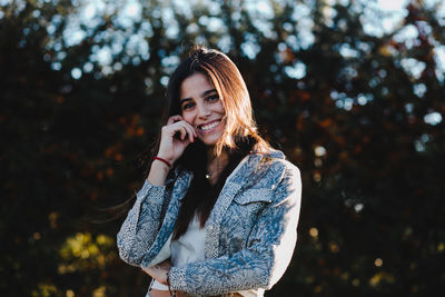 Portrait of smiling teenage girl standing against trees in park