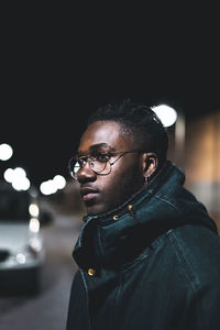 Close-up of man wearing eyeglasses in illuminated city at night