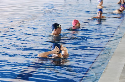 Group of people in swimming caps standing in pool during water aerobics class