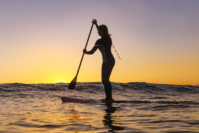 Female sup surfer at sunset time