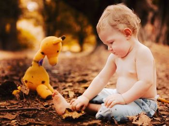 Cute toddler boy sitting near yellow toy on field