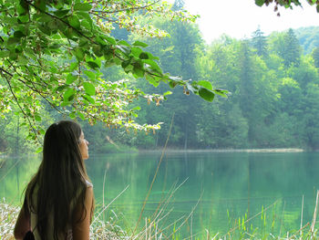 Rear view of woman standing by lake against trees