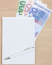High angle view of pen and note pad with various euro notes on table