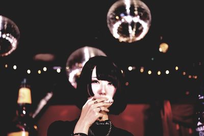 Portrait of young woman holding illuminated lighting equipment at night