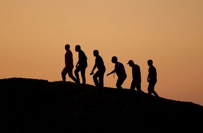 Silhouette people on rock against sky during sunset