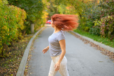 Side view of young woman standing against trees