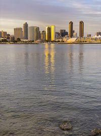 Sea by modern buildings in city against sky