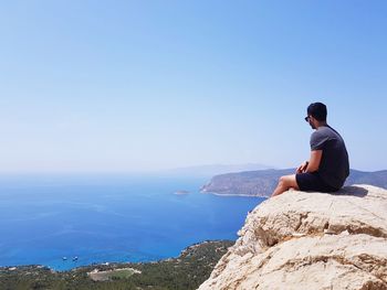 Man sitting on rock looking at sea against sky