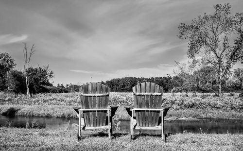 Chairs on field by trees against sky