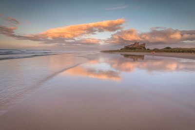 Scenic view of wet beach against sky during sunset