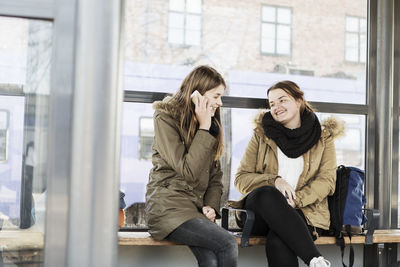 Young woman looking at female friend using mobile phone at train station