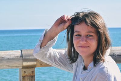 Portrait of smiling young woman holding sunglasses against sea