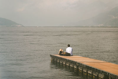 Rear view of couple sitting on sea shore against sky