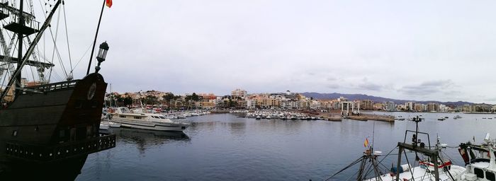 Boats moored at harbor against sky in city