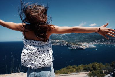 Rear view of woman with arms raised standing in sea