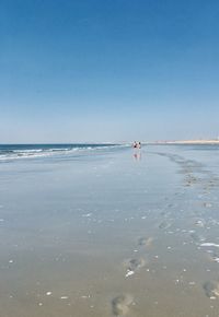 Scenic view of sea with a couple walking on beach 