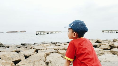 Rear view of boy on rocky shore against sky