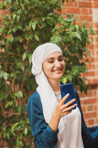 Portrait of a smiling young woman using phone while standing outdoors