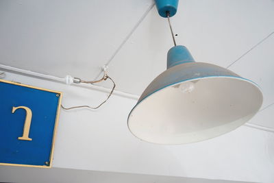 Low angle view of lighting equipment hanging against white wall