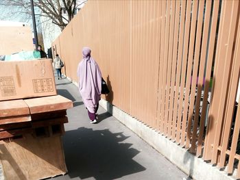 Full length rear view of woman walking on sidewalk by brown fence